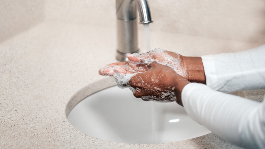 A pair of hands lathering with soap underneath a running faucet.