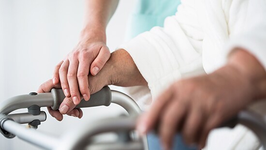  Close up of elderly hands holding walker with hands of healthcare provider helping. 