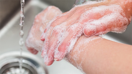 Two hands washing under running water with soap as part of the Ecolab Hand Hygiene Program.