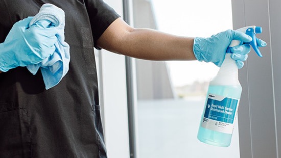 Hospitality employee cleaning a window with an Ecolab product