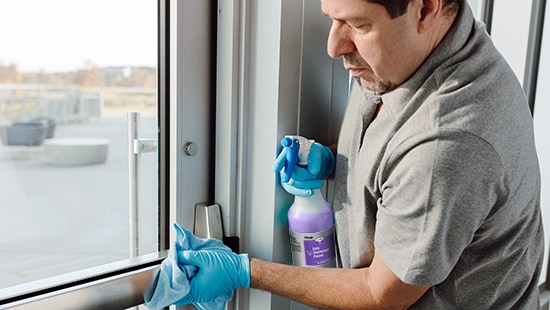 Custodian cleaning a door with an Ecolab product
