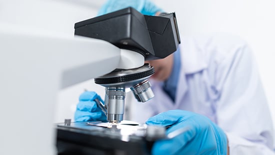 Biopharmaceutical technician looking through a microscope in a cleanroom