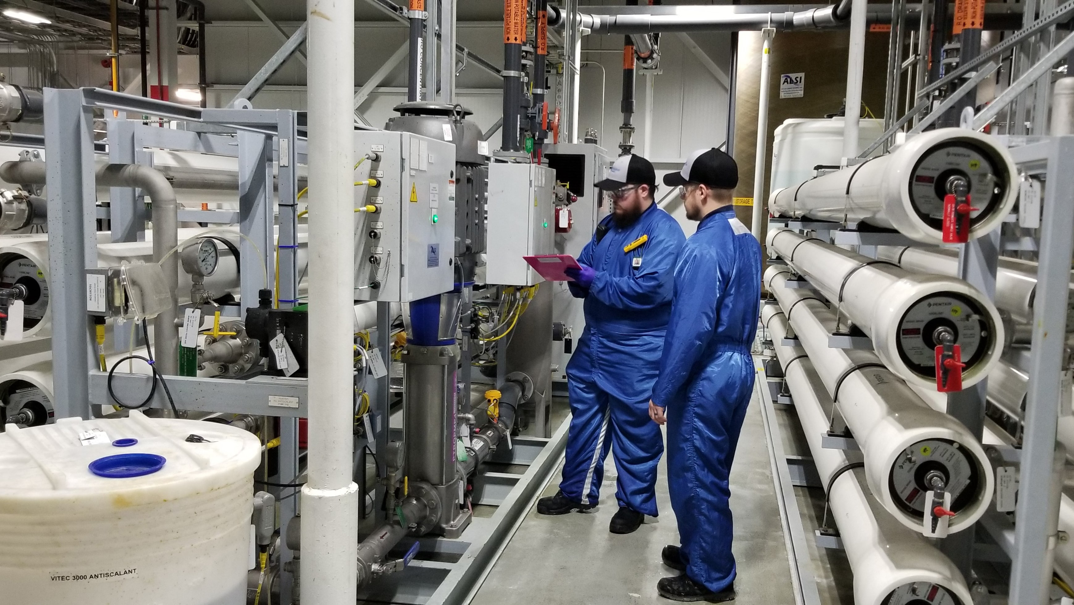 Two men standing near reverse osmosis system in industrial plant checking machine 