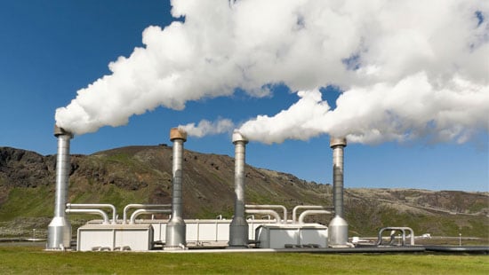 Exhaust pipes pushing mist out of a geothermal power plant from the bottom of a valley.