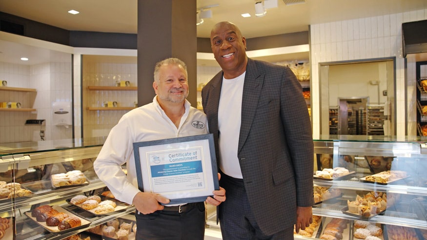 Raul Porto (left), owner of Porto’s Bakery in southern California, with Earl “Magic” Johnson (right). Porto is holding a framed certificate of commitment that demonstrates Porto's Bakery has earned the Ecolab Science Certified seal.