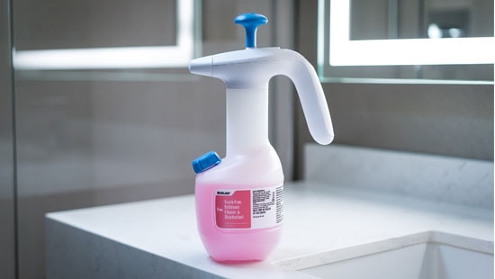 Ecolab scrub free hospital grade disinfectant bottle with air pump and pink fluid on top of a white counter 