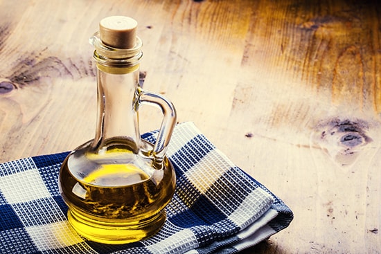 A glass bottle of olive oil placed on top of a kitchen rag on a wooden table. 