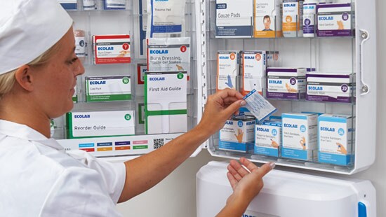 Health technician going through a first aid cabinet filled with first aid supplies.
