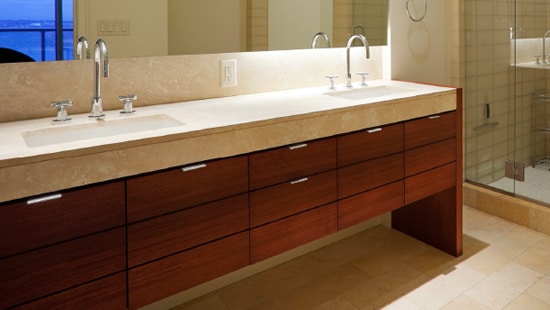 Hotel bathroom with two sinks and a large countertop with a standing shower and wooden drawers.