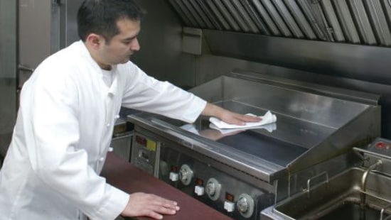 Chef wiping the top of a flat grill surface with a paper towel and Ecolab high-temp grill cleaner.