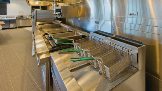 Clean and sanitized stainless steel fryer stations organized in a row of in a commercial kitchen.