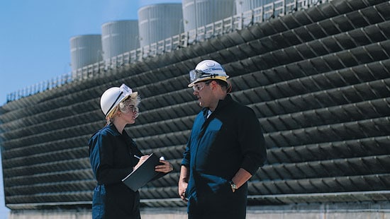 Two Workers Talking In Front of Cooling Towers