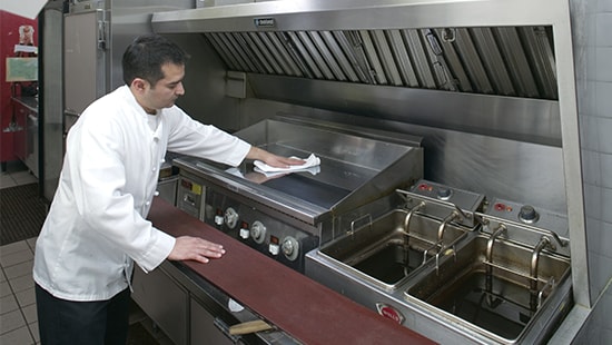 Chef Cleaning Grill Chef cleaning a stainless-steel grill from grease residue in a commercial kitchen.