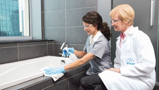 housekeeping employee in a training program with instructor spraying and wiping a bathtub clean 