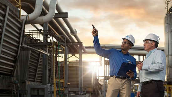 Two men standing outside and pointing at cooling tower and related water treatment systems.