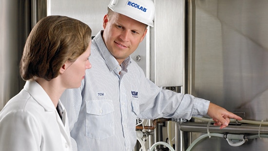 An Ecolab expert is pointing at a machine while speaking to an employee at a food processing facility.
