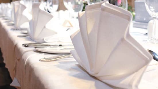 A dining table covered with a white tablecloth and white table napkins, plates, and glassware. 