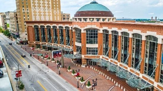 Aerial view of a large brick convention center with tall windows and a domed roof along a city street.