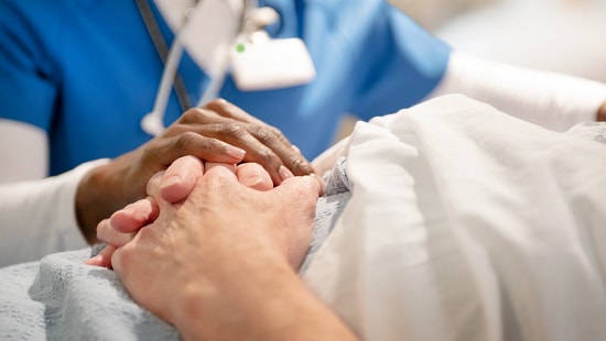 A healthcare worker's hands resting upon a patient's hands.