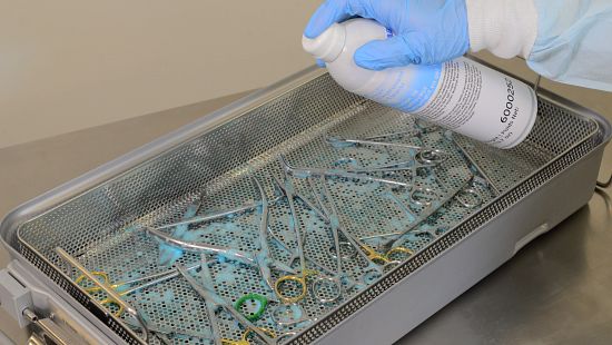 Gloved hand using Ecolab product to safely clean surgical scissors.