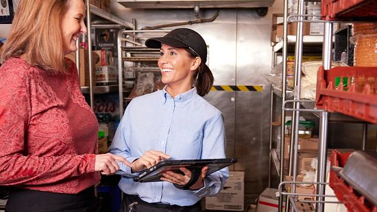 Restaurant manager and employee review inventory and operations in back-of-house storage area