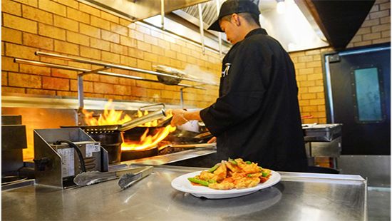 Chef cooks a hot meat at workstation in a Fast- casual restaurant kitchen.