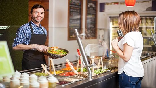 Food service employee assembles a fresh salad from a self -service ingredient bar
