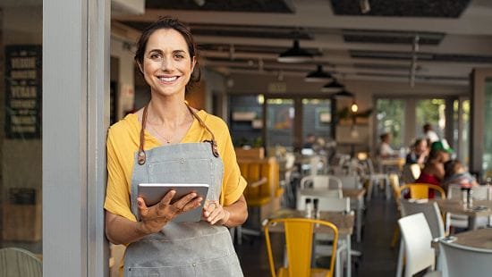 Front of House waitstaff standing in restaurant entranceway holding a tablet and smiling.