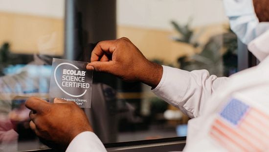 Restaurant worker sticking an Ecolab Science Certified sticker on the front of a restaurant window.
