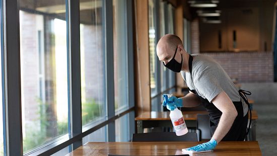 Sink and Surface Cleaner Sanitizer in spray bottle in use by waiter/busser wearing gloves at restaurant table