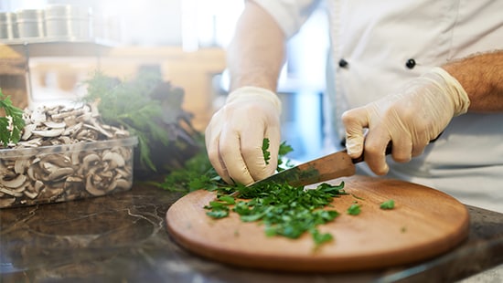 Restaurant Chef Wearing Food Safety Gloves and Chopping Parsley inside a Restaurant Kitchen. 