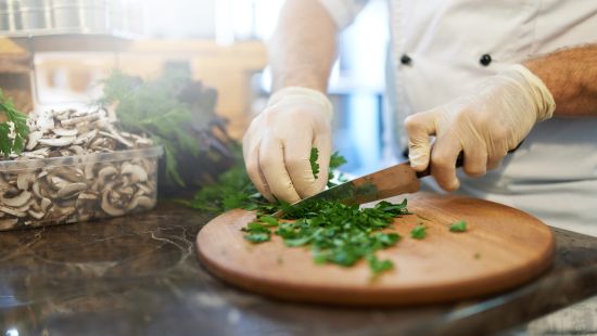 Chef with plastic gloves chopping parsley on wooden cutting board.