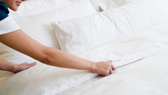 Housekeeper making the bed by fixing pillows and pressing sheets of in a hotel room