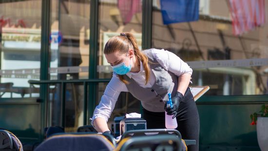 Ecolab Science Certified program restaurant worker in protective mask cleaning a patio table.
