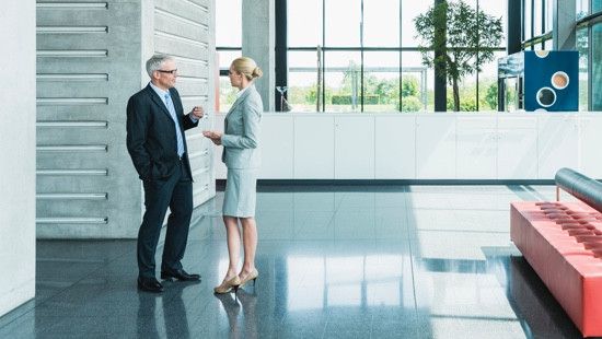 Two business professionals talking in an empty lobby with large windows and chic furniture.