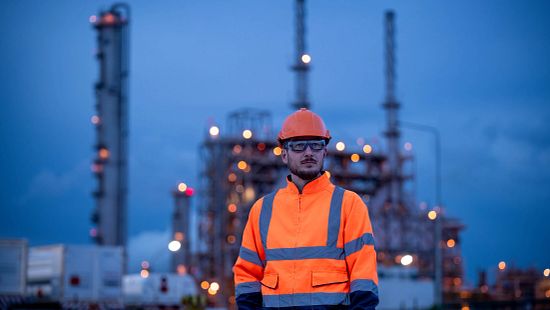 An engineer wearing a uniform, glasses and helmet  on a plant site with night lights in the background.