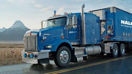 Massive freight truck driving on a wet mountain road loaded with mobile water equipment.