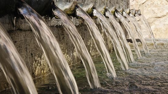 Water flowing out of large pipes in a cement wall into a body of water