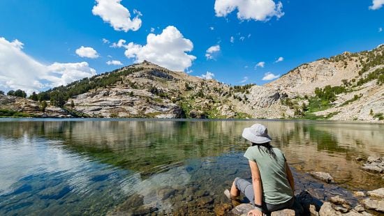 Shutterstock 1799719549 woman on a still lake with mountains