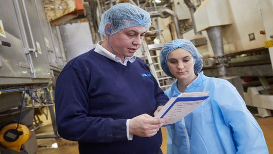 Supervisor and employee in hairnets talking in food and beverage processing facility.